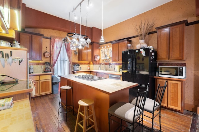 kitchen with a center island, sink, stainless steel appliances, decorative light fixtures, and a kitchen bar