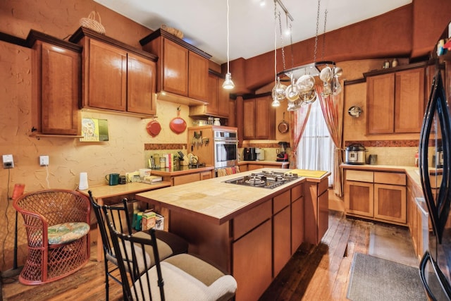 kitchen with black fridge, a kitchen island, dark hardwood / wood-style floors, and stainless steel gas stovetop