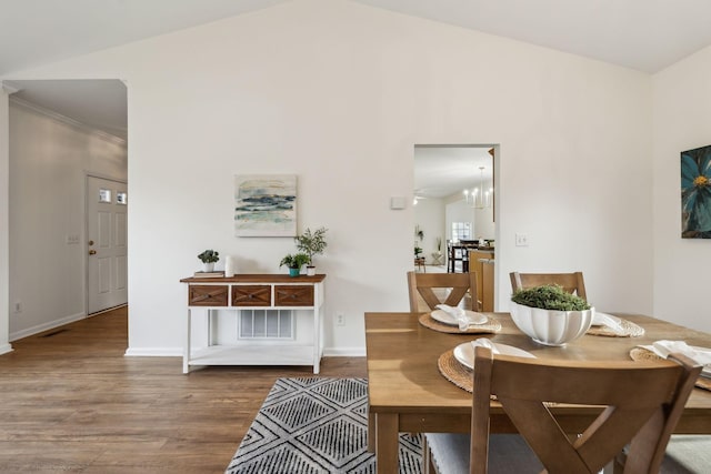 dining space featuring a chandelier, crown molding, wood-type flooring, and lofted ceiling