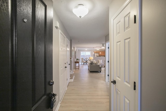 hall with a textured ceiling and light wood-type flooring