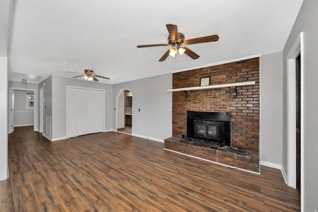 unfurnished living room with a textured ceiling, a wood stove, ceiling fan, and dark wood-type flooring