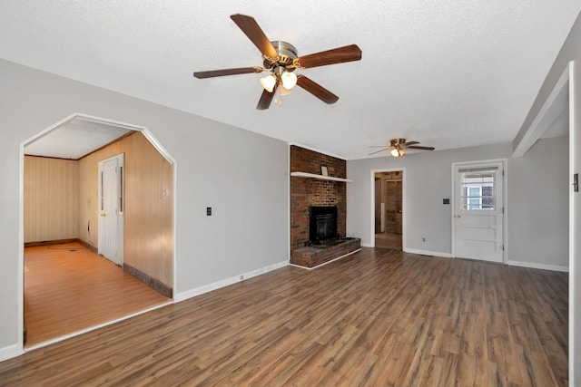 unfurnished living room featuring wooden walls, ceiling fan, a textured ceiling, a fireplace, and wood-type flooring