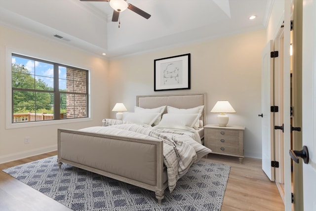 bedroom featuring ceiling fan, a raised ceiling, light wood-type flooring, and ornamental molding