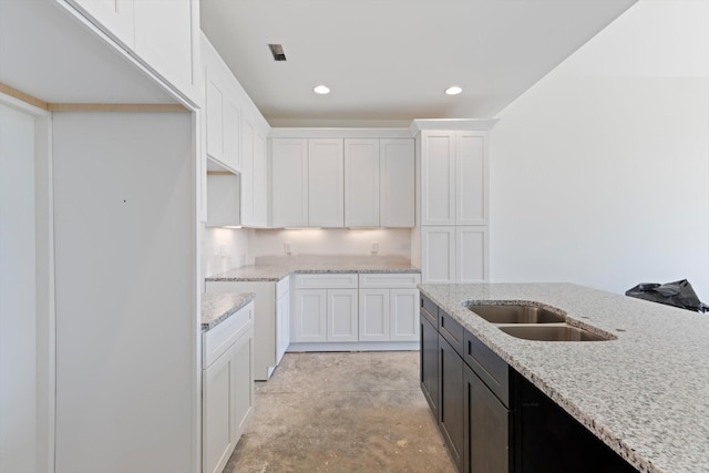 kitchen with white cabinetry, light stone counters, and sink