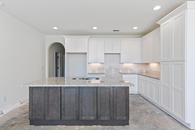 kitchen featuring white cabinetry, an island with sink, and light stone counters