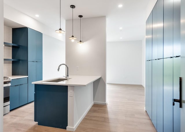 kitchen with kitchen peninsula, stainless steel range, sink, blue cabinetry, and hanging light fixtures