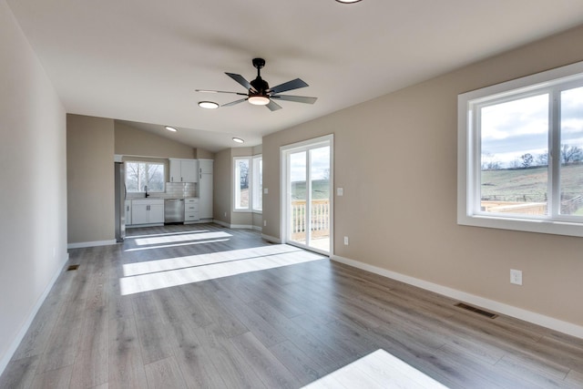 unfurnished living room featuring ceiling fan, sink, light hardwood / wood-style floors, and lofted ceiling