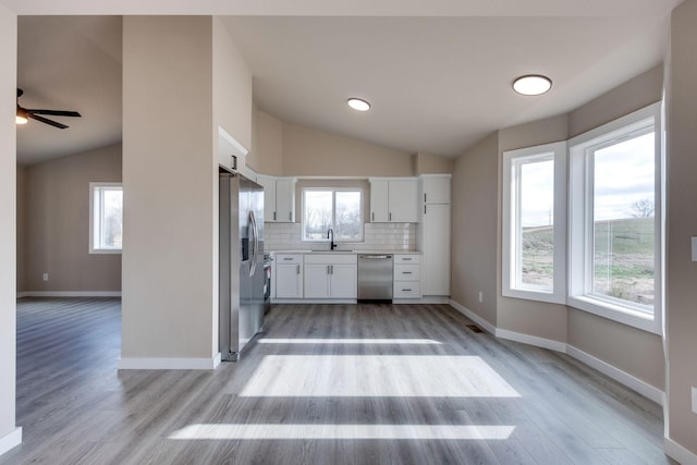 kitchen featuring white cabinetry, stainless steel appliances, light hardwood / wood-style floors, lofted ceiling, and decorative backsplash