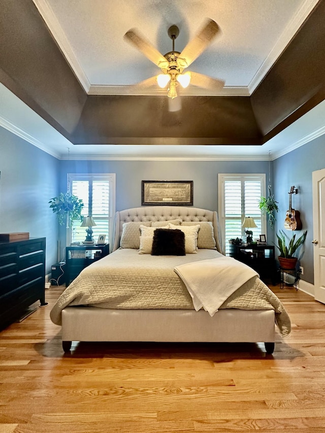 bedroom featuring a raised ceiling, multiple windows, ceiling fan, and light hardwood / wood-style flooring