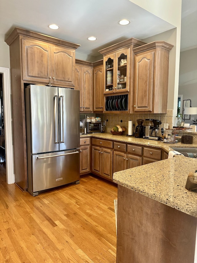 kitchen with stainless steel refrigerator, light stone countertops, tasteful backsplash, light hardwood / wood-style flooring, and kitchen peninsula