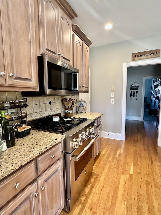 kitchen featuring light stone countertops, appliances with stainless steel finishes, light wood-type flooring, and tasteful backsplash