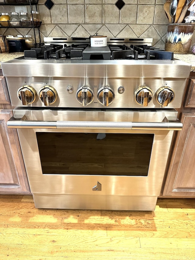 room details featuring decorative backsplash, light stone countertops, light hardwood / wood-style floors, and high end stainless steel range