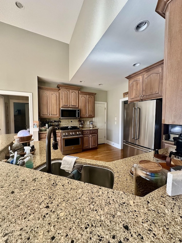 kitchen with sink, light stone counters, backsplash, high quality appliances, and light wood-type flooring