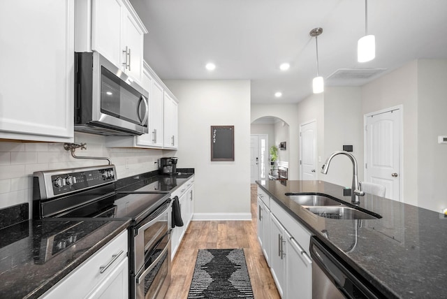 kitchen with stainless steel appliances, sink, decorative light fixtures, dark stone countertops, and white cabinetry