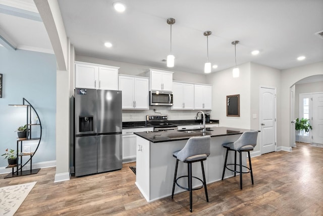 kitchen featuring white cabinets, a center island with sink, sink, decorative light fixtures, and stainless steel appliances