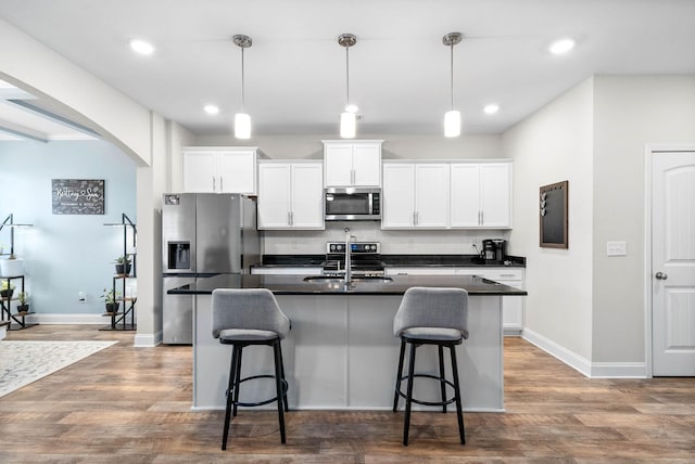 kitchen with sink, stainless steel appliances, hanging light fixtures, and an island with sink