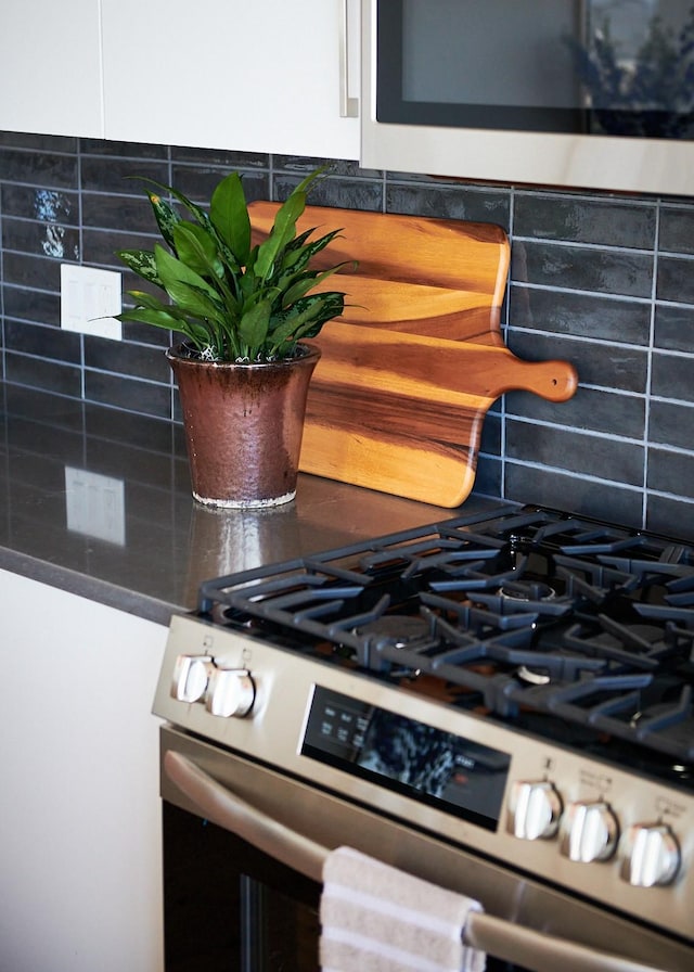 interior details with white cabinets, stainless steel gas stove, and backsplash