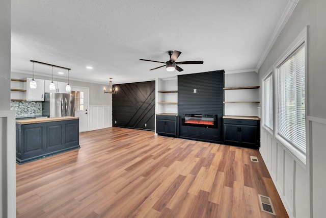 unfurnished living room featuring light wood-type flooring, crown molding, a fireplace, a textured ceiling, and ceiling fan with notable chandelier