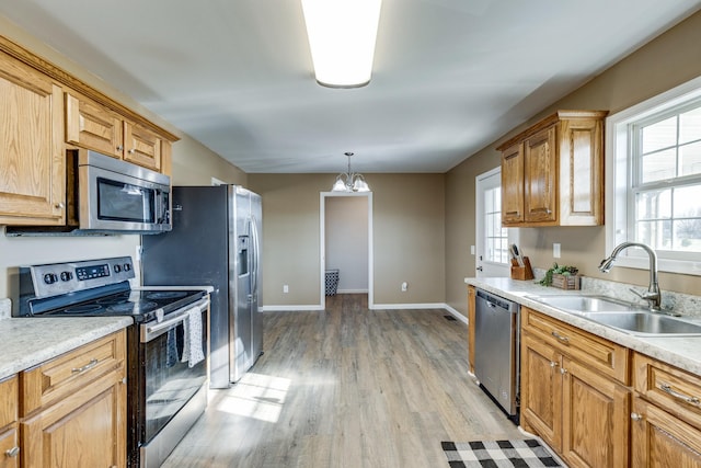 kitchen featuring pendant lighting, sink, light hardwood / wood-style flooring, stainless steel appliances, and a chandelier