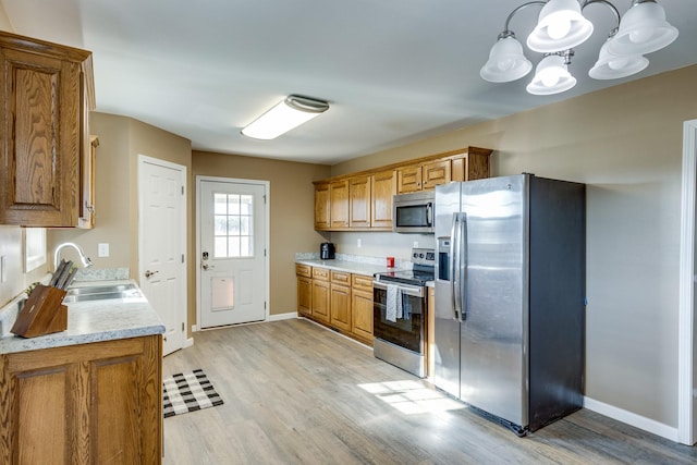 kitchen with appliances with stainless steel finishes, light wood-type flooring, sink, decorative light fixtures, and a notable chandelier