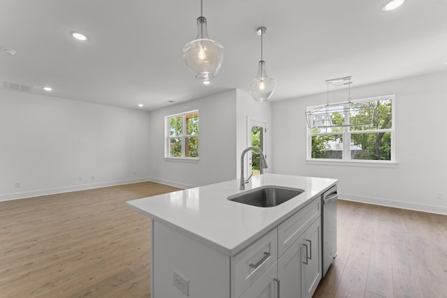 kitchen with decorative light fixtures, dishwasher, light hardwood / wood-style floors, a center island with sink, and sink