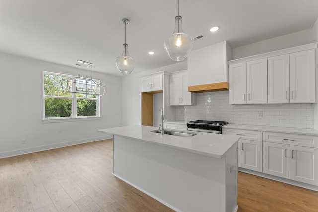 kitchen with stainless steel range with electric cooktop, white cabinetry, and a center island with sink