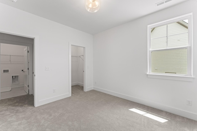 unfurnished bedroom featuring a spacious closet, a closet, and light colored carpet