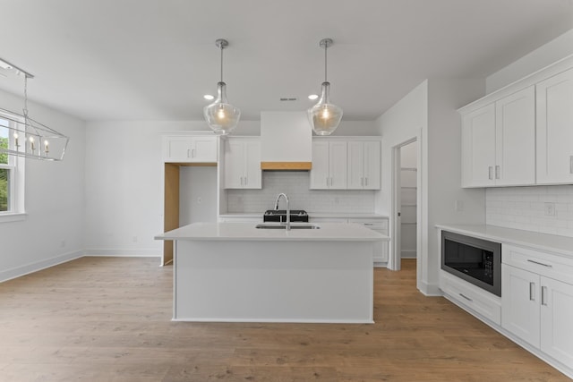 kitchen featuring white cabinetry, an island with sink, black microwave, and custom exhaust hood