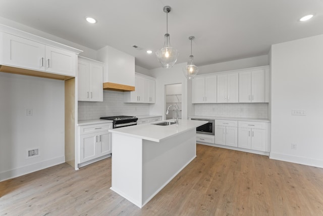 kitchen featuring an island with sink, backsplash, hanging light fixtures, white cabinets, and sink