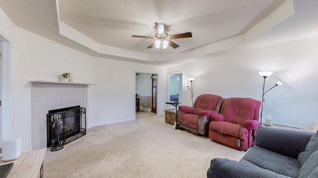 living room featuring a tray ceiling, ceiling fan, carpet flooring, and a textured ceiling