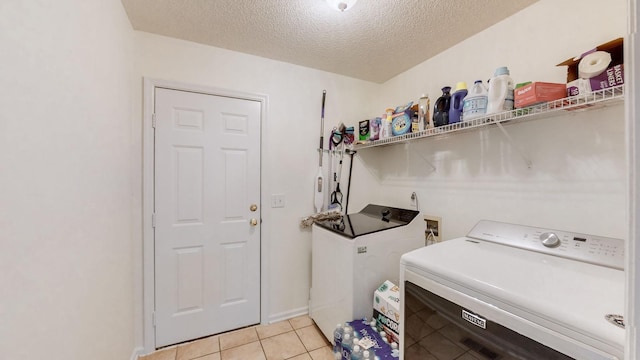 laundry room featuring separate washer and dryer, light tile patterned floors, and a textured ceiling