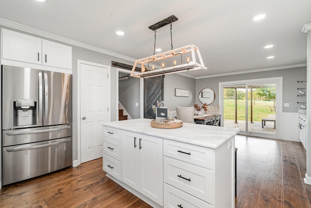 kitchen featuring stainless steel fridge, a barn door, white cabinetry, and hanging light fixtures