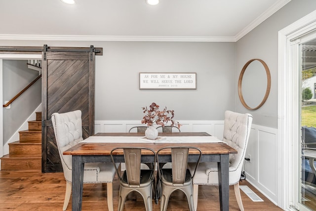 dining space featuring a barn door, wood-type flooring, and ornamental molding