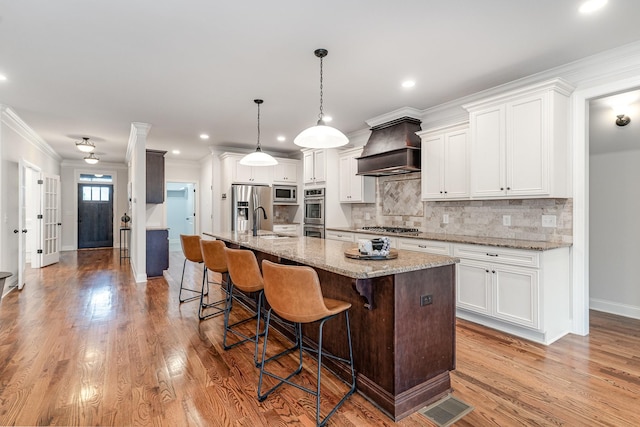 kitchen with white cabinets, stainless steel appliances, a kitchen island with sink, and custom exhaust hood