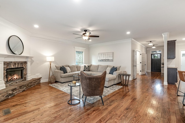 living room with hardwood / wood-style flooring, ceiling fan, a stone fireplace, and crown molding