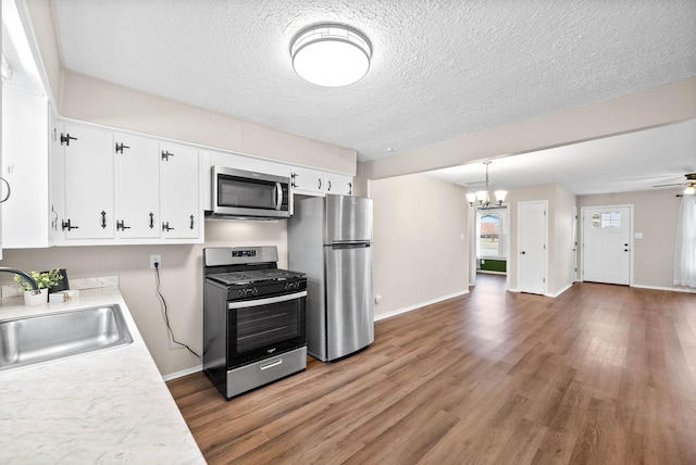 kitchen featuring white cabinetry, sink, hanging light fixtures, stainless steel appliances, and ceiling fan with notable chandelier