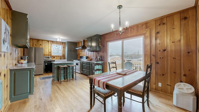 dining space featuring an inviting chandelier, sink, wooden walls, and light hardwood / wood-style floors