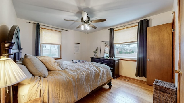 bedroom featuring multiple windows, heating unit, ceiling fan, and light wood-type flooring