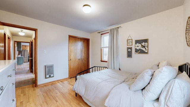 bedroom with stainless steel refrigerator, a closet, light hardwood / wood-style floors, and heating unit