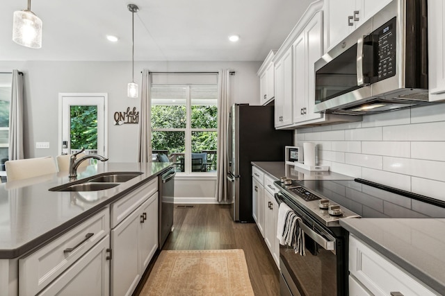 kitchen with appliances with stainless steel finishes, dark wood-type flooring, sink, pendant lighting, and white cabinetry