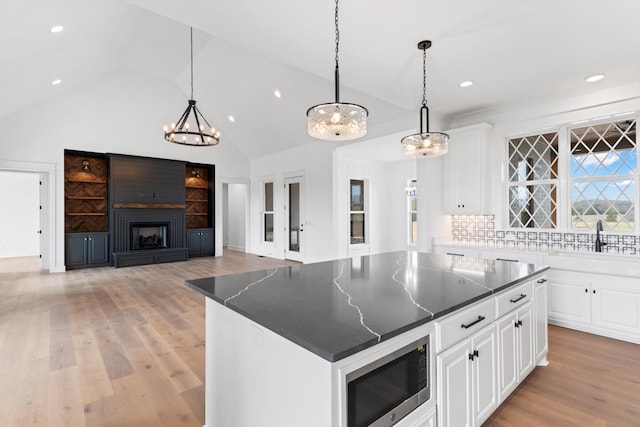 kitchen featuring built in microwave, a large fireplace, white cabinets, decorative backsplash, and a kitchen island