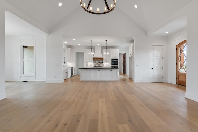 unfurnished living room with high vaulted ceiling, light hardwood / wood-style floors, and a notable chandelier