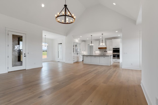 unfurnished living room with light hardwood / wood-style floors, sink, high vaulted ceiling, and an inviting chandelier