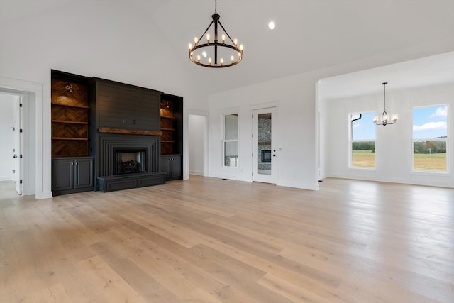 unfurnished living room with a fireplace, light wood-type flooring, vaulted ceiling, and a notable chandelier