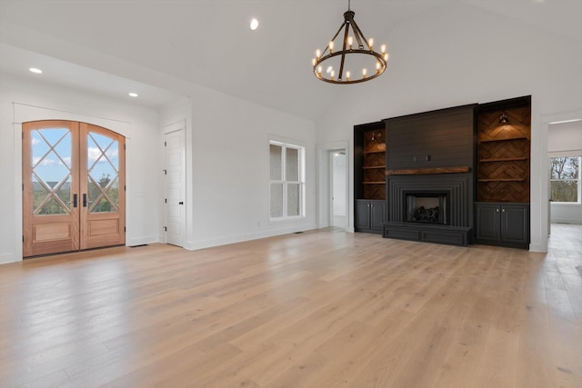 unfurnished living room featuring a large fireplace, light hardwood / wood-style flooring, an inviting chandelier, and high vaulted ceiling