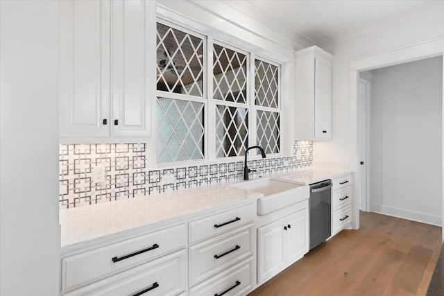 kitchen featuring light wood-type flooring, tasteful backsplash, stainless steel dishwasher, sink, and white cabinetry