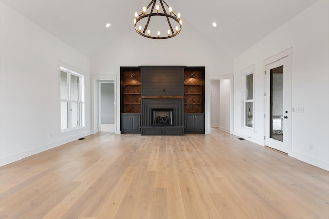 unfurnished living room featuring a notable chandelier, light hardwood / wood-style floors, a fireplace, and high vaulted ceiling