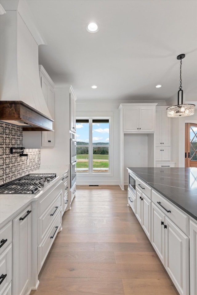 kitchen featuring light wood-type flooring, custom range hood, stainless steel appliances, pendant lighting, and white cabinets