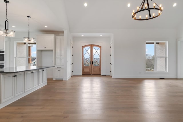 foyer with plenty of natural light, high vaulted ceiling, light wood-type flooring, and a notable chandelier