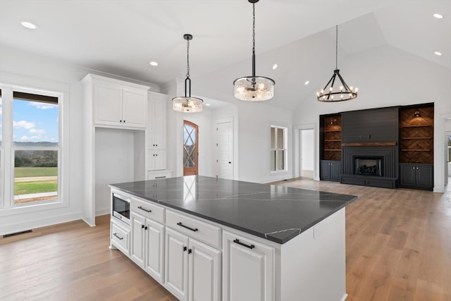 kitchen with white cabinetry, a large fireplace, a kitchen island, and pendant lighting